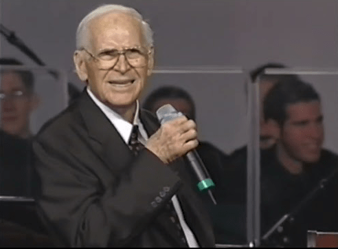 Elderly man holding a microphone.