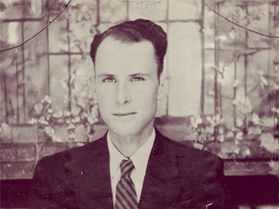 Vintage sepia portrait of a young man in a suit and tie, with a serious expression, set against a blurred floral backdrop. Tone is formal and timeless.